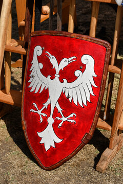 Medieval red heater shield with a painted white double-headed eagle emblem leaning against a wooden rack