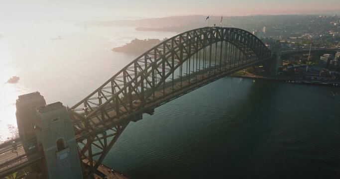 Iconic Sydney Harbour Bridge connecting city districts, bathed in warm morning light, with the city skyline and harbor extending into the distance. Dramatic evening light. Aerial view drone flight