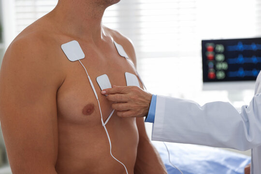 Doctor attaching ECG electrodes to patient's chest in clinic, closeup