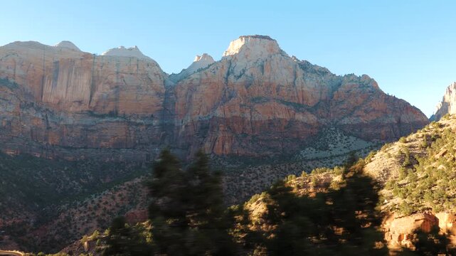 Stunning mountain scenery of zion national park in utah filmed from moving vehicle, showing majestic red rock formations and steep sandstone cliffs under a clear blue sky during a sunny day. Road trip