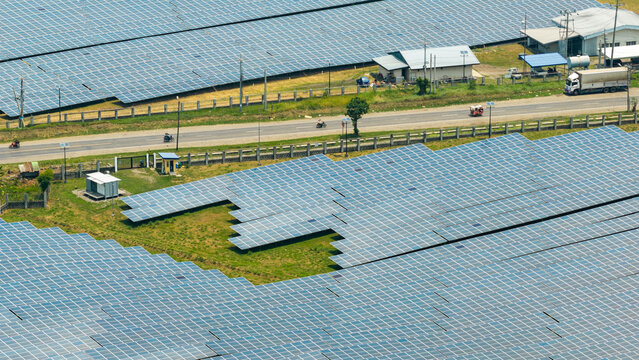 Bais City, Negros Island Region, Philippines - 20 September 2026: Aerial view of a solar farm with rows of photovoltaic panels, a nearby road with vehicles, and small utility buildings.