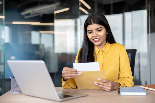 Indian businesswoman receiving good news, opening a letter and smiling in a modern office, symbolizing success, promotion, and professional achievement