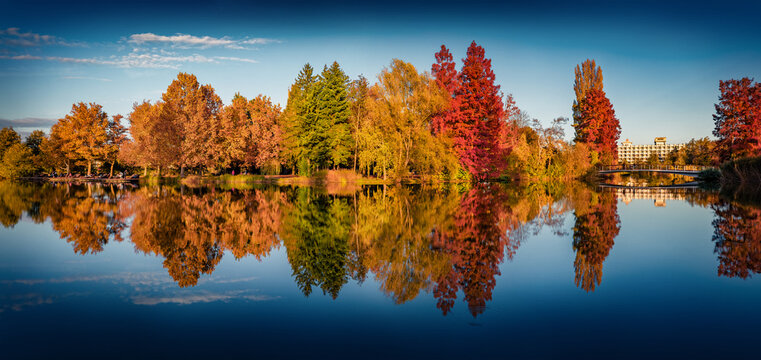 Panoramic autumn view of Boating Island in Szombathely town, administrative centre of Vas County, Hungary. Calm afternoon scene of Boating lajke. Trees covered with orange and crimson leaves.
