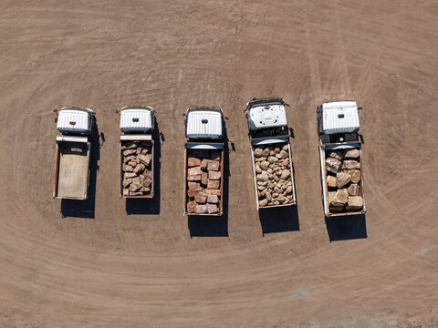 Kilsyth, Australia - 20 September 2026: Aerial view of five dump trucks parked in a row on a dirt lot, with some vehicles loaded with large rocks and others empty.