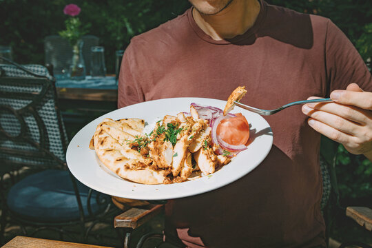 Man enjoying a chicken gyro plate with pita bread, tomato, and onion outdoors, having a Mediterranean lunch