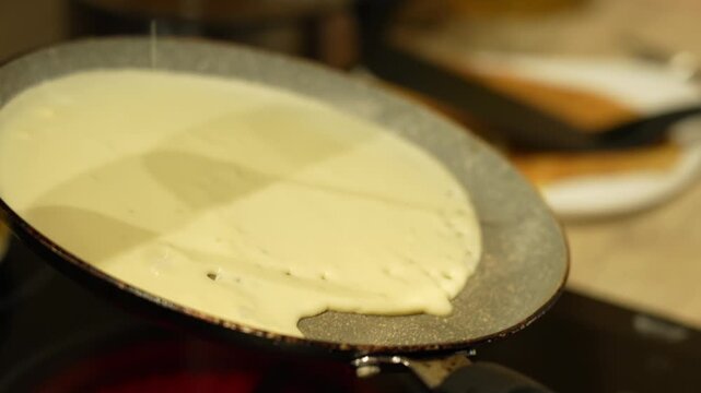 Creamy batter pours into a hot frying pan. The liquid spreads smoothly on the pan's surface. Hand guides the pouring motion. Ideal for cooking tutorials. Perfect for culinary content