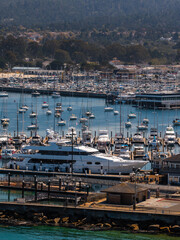 Fototapeta premium Aerial shot displays numerous sailboats, yachts, and leisure watercraft moored along the docks and marina in Monterey, California, with coastal buildings visible inland.