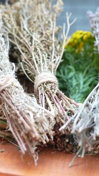 Dried lavender bundles tied with twine rest on wooden surface. Pale purple flowers stand out clearly. Soft focus shows green foliage behind. Natural texture suggests rustic charm