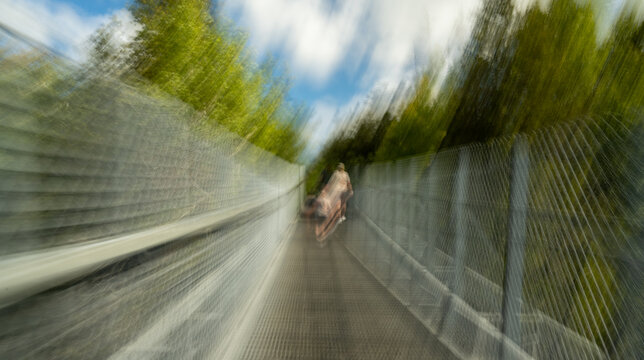 Multiple exposure and motion blur while walking across a suspension pedestrian bridge with white clouds in a blue sky

