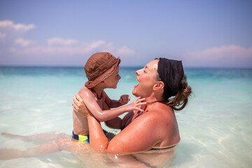 Fototapeta premium Mother and young son playing together in shallow sea during summer vacation
