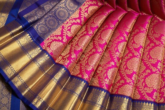Pink Kanchipuram pattu silk saree with broad gold zari border. Traditional Indian wedding garment features luxury floral patterns, ethnic motifs. Rich textile texture shows elegant craftsmanship of