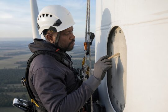 Wind turbine lightning protection inspection - a rope access inspector brushing a receptor