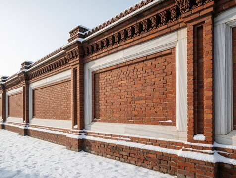 Ornate red brick wall with white marble frames in winter. Detailed masonry architecture covered in fresh snow. Classic decorative exterior structure with rustic patterns, stone texture. Cold seasonal