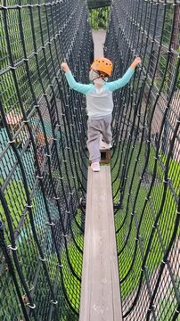  Child on narrow suspended rope bridge in adventure park &mdash; orange helmet (vertical)