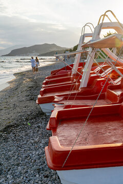 Row of red pedal boats with water slides parked on a pebble beach at sunset