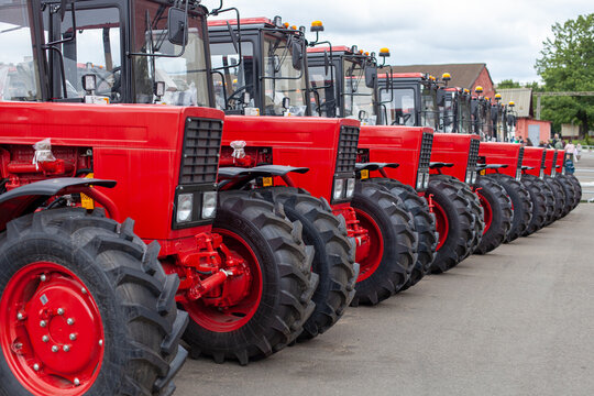 Row of new red tractors parked on asphalt. Industrial scale, agricultural supply, modern farming equipment, supply chain logistics.