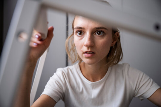 Smiling young woman using a screwdriver to assemble white flat-pack furniture frame. Focus on her hands and face with creative indoor workshop background. DIY home improvement and craftsmanship concep