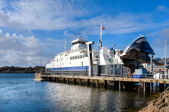 Large car ferry with its bow ramp open is docked at the ferry terminal in Svolvaer on the Lofoten Islands beneath clear blue sky.