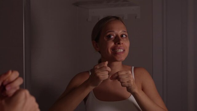 Young woman cleaning teeth with dental floss in bathroom mirror, focused oral hygiene routine, caring for gums and removing debris between teeth at home