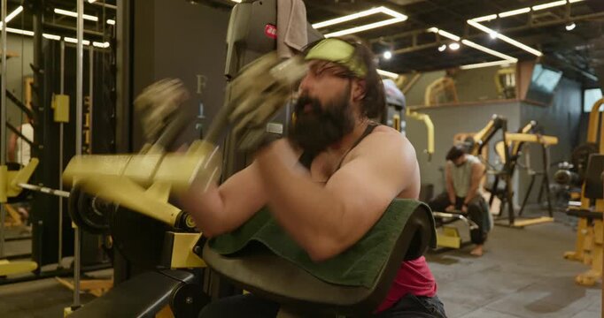 A fit Indian man trains his arms with dumbbells and resistance exercises at the gym. The fitness enthusiast performs controlled repetitions to develop arm strength, muscle mass, and definition