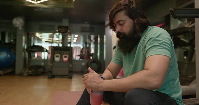 Indian male athlete taking a pre-workout drink before weight training at the gym. The fitness enthusiast gets energized and mentally prepared for a demanding workout