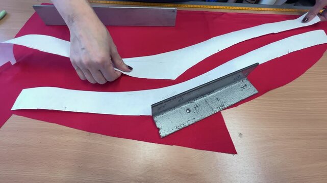 A woman carefully arranges paper pattern pieces on a vibrant red fabric, preparing for cutting. Her hands are focused on aligning the patterns with precision on a wooden table