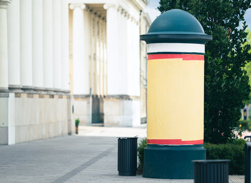 Blank advertising pillar on a city sidewalk next to a building with large white columns