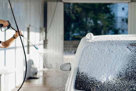 Worker cleaning a car with pressurized foam at a wash facility during the bright daylight hours