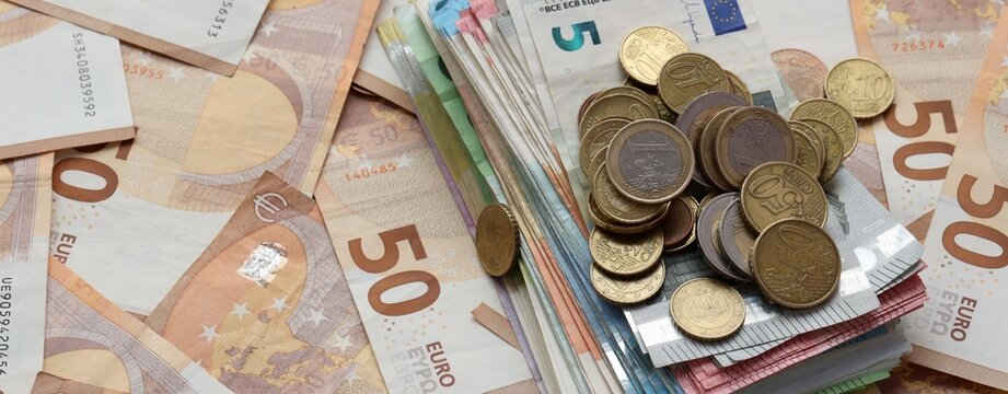 Pile of euro coins on stack of euro banknotes with fifty euro background