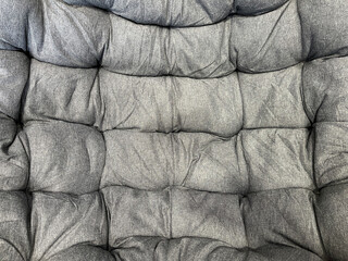 Obraz premium Close-up of a gray tufted fabric cushion with soft folds, stitched sections, and textured upholstery, creating a cozy abstract background pattern.