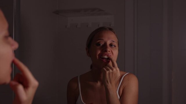 Young woman applying medicated dental gel to gums and teeth in the mirror, caring for mouth irritation during a home routine
