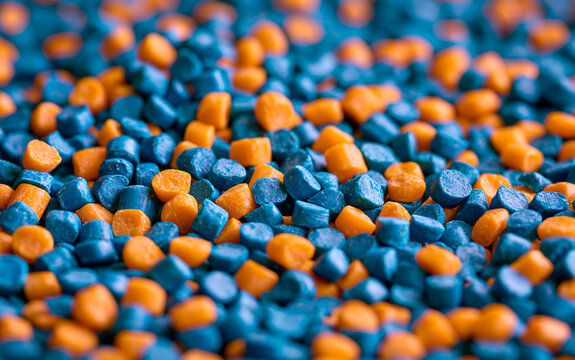 Close up of blue, orange plastic granules. Colorful polymer resin pellets pile up for industrial injection moulding process. Raw thermoplastic material beads used in manufacturing production