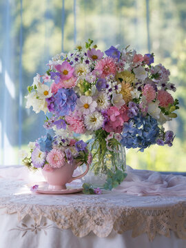 Beautiful bouquet in a vase flowers phlox, asters, hydrangeas and bellflowers on a table, cup and saucer, still life set against a window overlooking the garden.