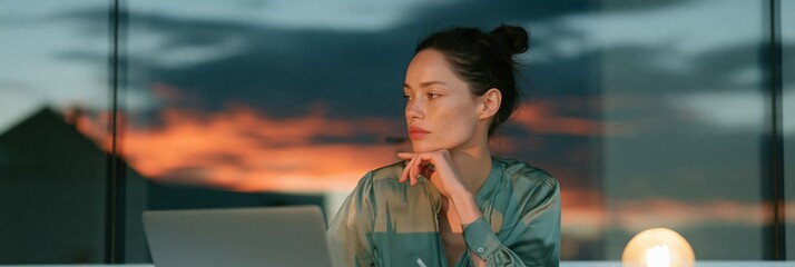 Obraz premium Woman working at laptop looking thoughtful during sunset through a window for remote work background and contemplative business banner
