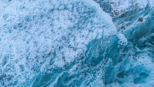 Detailed blue seascape texture featuring rolling surf, frothy foam, delicate sea spray, and dramatic patterns created by the moving water.