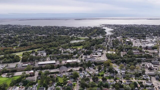 A drone pans across Babylon on Long Island toward Great South Bay in New York. Marinas and waterfront neighborhoods meet calm waterways while parkland and tree lined streets fill the foreground below.