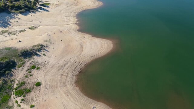 Aerial view of a drying reservoir with receded water levels exposing arid, cracked soil due to extreme drought and climate change
