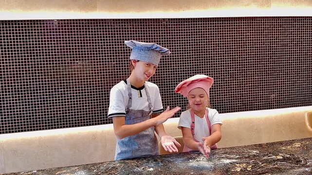 Two little chefs clapping floury hands over kitchen counter (horizontal)