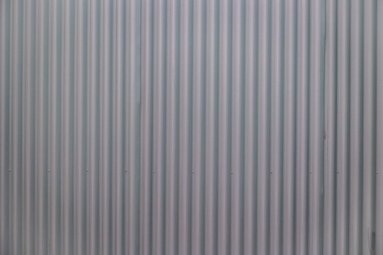 Detailed gray metal siding featuring parallel vertical grooves, subtle shadows, regular screws, and a minimalist contemporary building exterior.