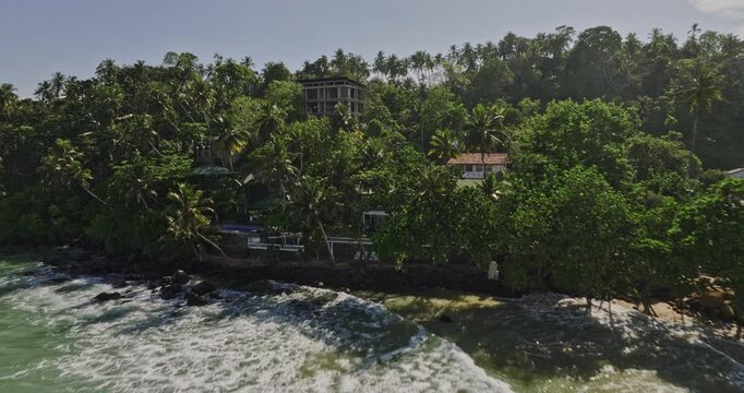 Mirissa Sri Lanka Aerial v7 fly along sandy beach capturing crashing waves, beachfront resort hotel and restaurants, flyover the hill reveals sweeping oceanscape - Shot with Mavic 3 Cine - April 2023