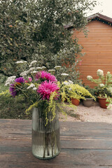 Autumn bouquet of pink asters and goldenrod in glass vase on wooden table © emerald17