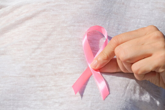 Woman in white linen dress holding pink ribbon during breast cancer awareness campaign event outdoors