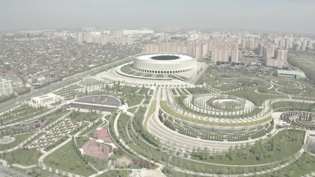 Aerial panorama of circular urban plaza with concentric tree rings and central ponds under overcast daylight emphasizing geometric symmetry and landscape layout