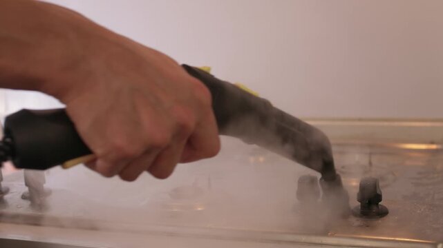 Handheld steam cleaner on stove top, powerful steam loosening burnt grease from stainless surface, closeup of nozzle and hand motion, countertop background, satisfying deep clean