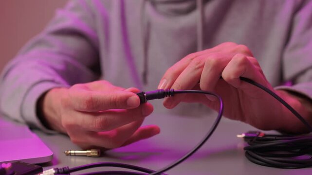 Individual carefully manipulating audio adapters at workspace during setup. Technician meticulously inspecting and fitting audio connectors with ambient lighting at desk
