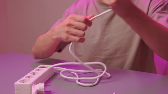 Neat electrical connection demonstration. Hands carefully connecting cords to power source. Detailed scene of person organizing wires on colorful illuminated desk surface