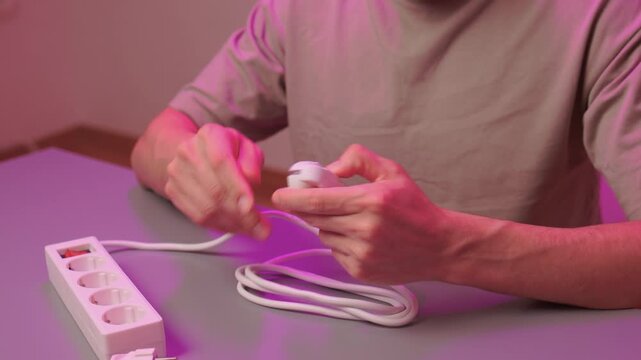 Neat electrical connection demonstration. Hands carefully connecting cords to power source. Detailed scene of person organizing wires on colorful illuminated desk surface