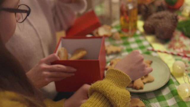 Warm lifestyle footage shows two women who pack homemade cookies into a festive red box together. Close lifestyle view conveys creative gift giving in a polished lifestyle scene.