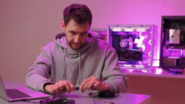 Hands connecting external sound card to laptop, audio technician tests input adjusts knob and toggles controls while cable rests on desk under purple mood lighting