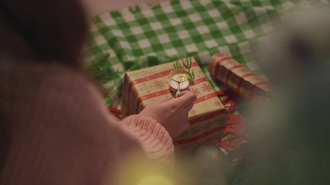 Warm Christmas footage presents a wrapped present with a round wax seal beside warm candlelight. Festive flat lay view captures elegant handmade packaging for authentic Christmas storytelling.
